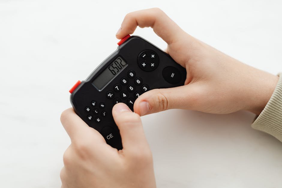Close-up of hands using a portable black calculator with a digital display on a white background.
