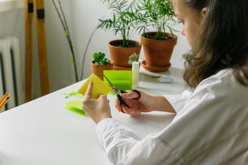 Teenager working on a creative DIY project, cutting paper with scissors, surrounded by potted plants.