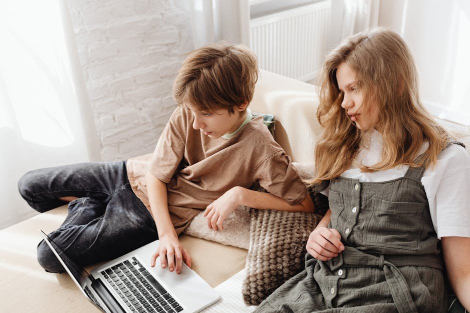 Kids relaxing on a sofa using a laptop together at home, enjoying leisure time.