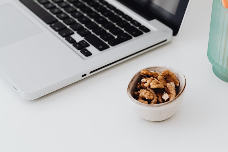 A minimalistic work desk setup featuring a laptop and a bowl of healthy walnuts for snacking.