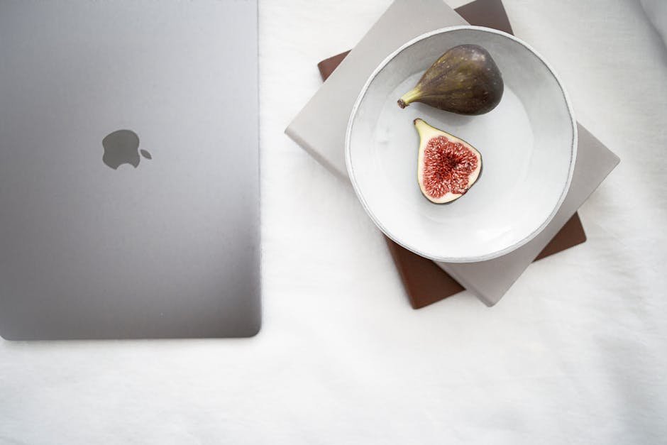 From above plate of fresh ripe exotic fig fruit placed on notebooks near modern laptop on white comfortable bed