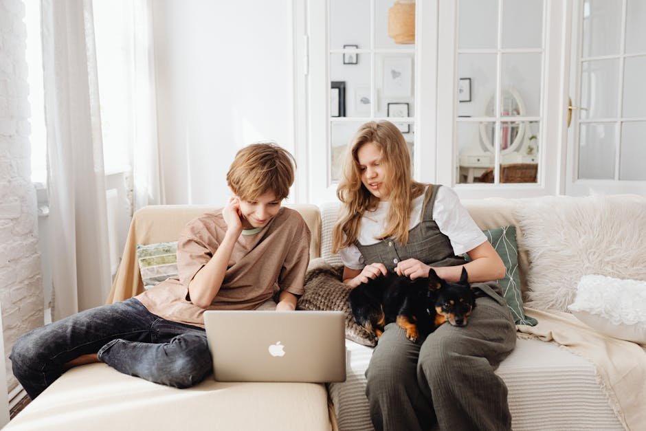 Brother and sister with their dog using a laptop on the sofa, enjoying togetherness at home.