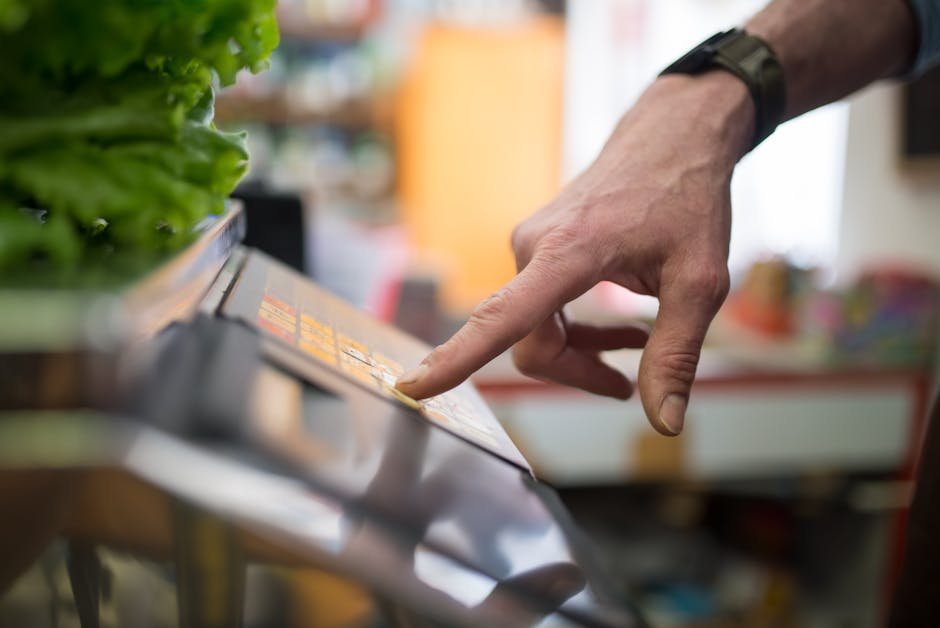 A hand interacting with a digital weighing scale in a produce section, emphasizing technology in shopping.