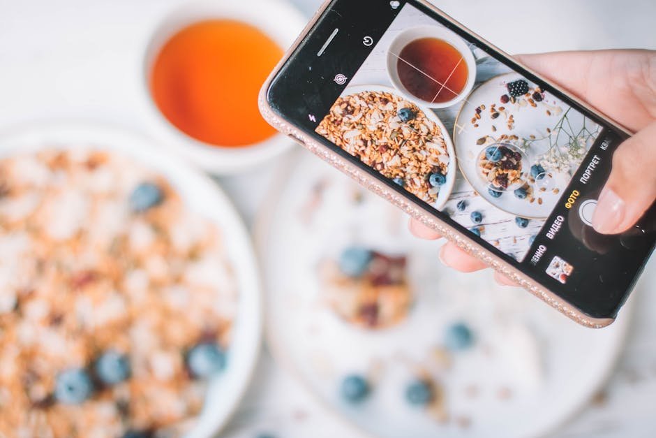 A smartphone capturing a healthy breakfast bowl with blueberries and tea.